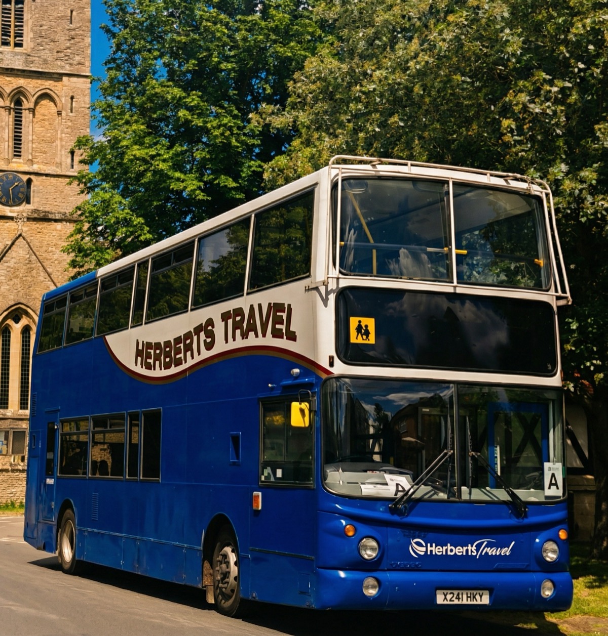 A Herberts Travel double-decker parked beside a village church