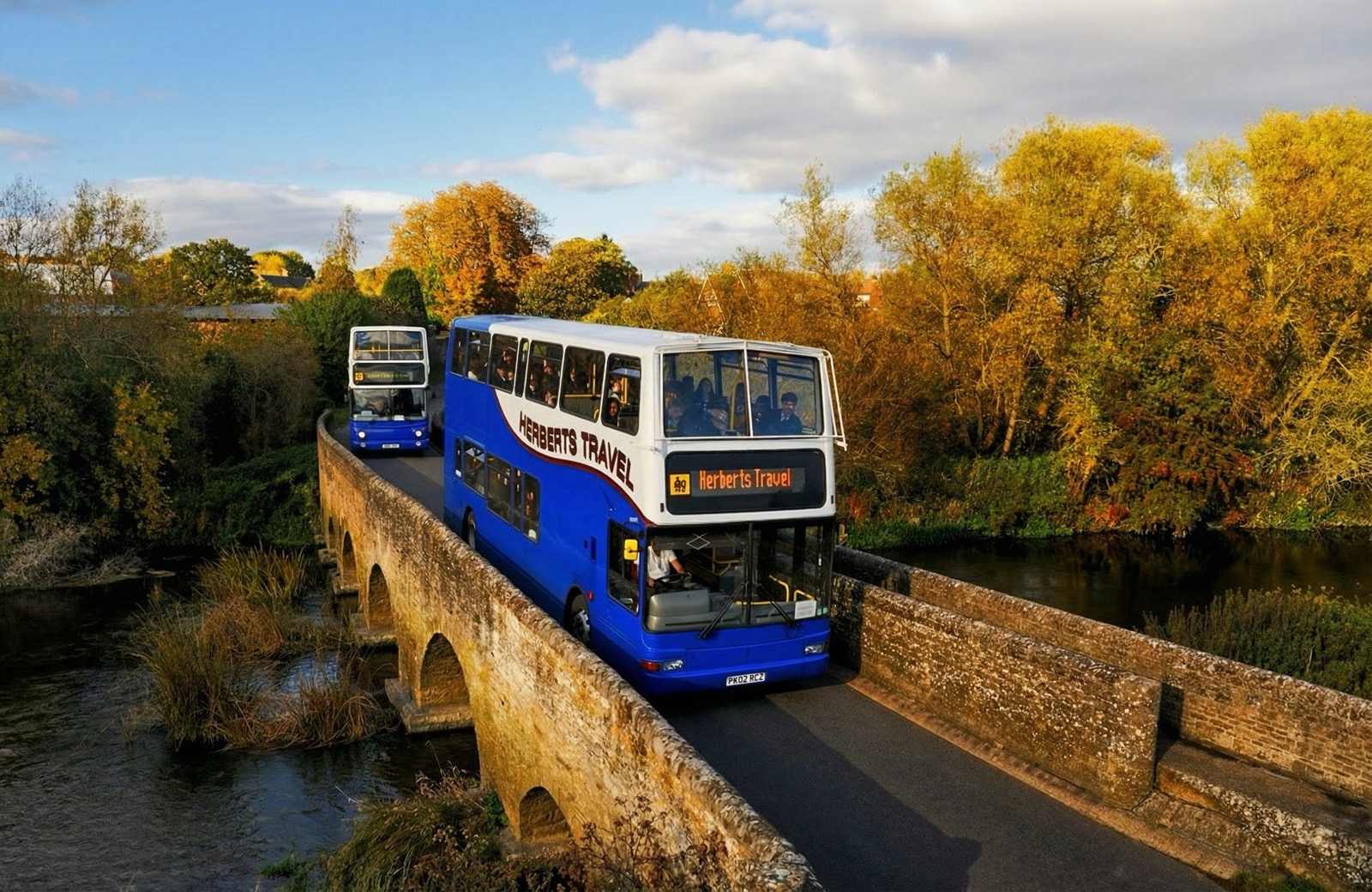 Two Herberts Travel double-deckers crossing a stone bridge in autumn